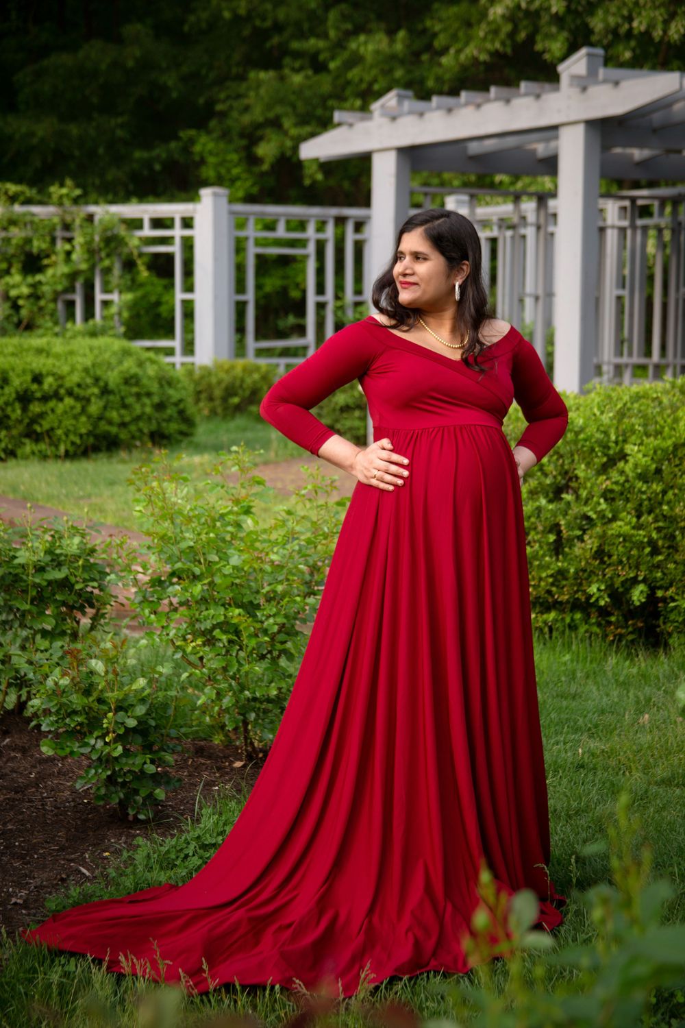 Pregnant woman stands strong wearing a long red gown during maternity photography session.