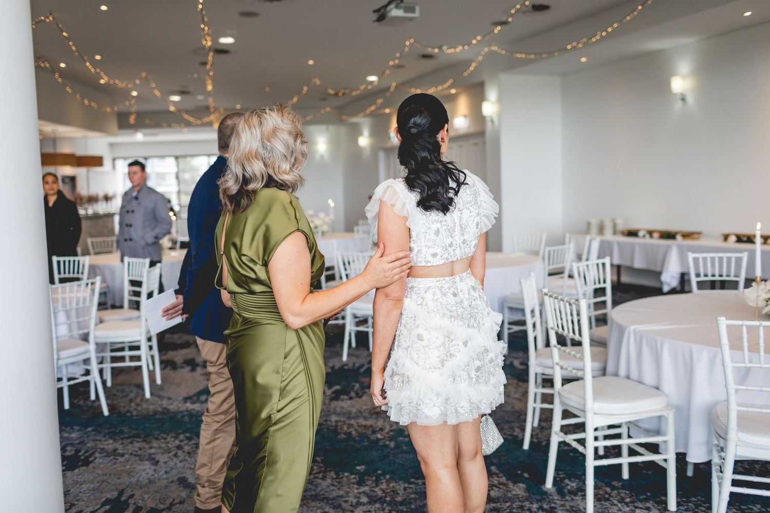 Wedding celebration scene in light-filled room with white chairs and blue carpeting.