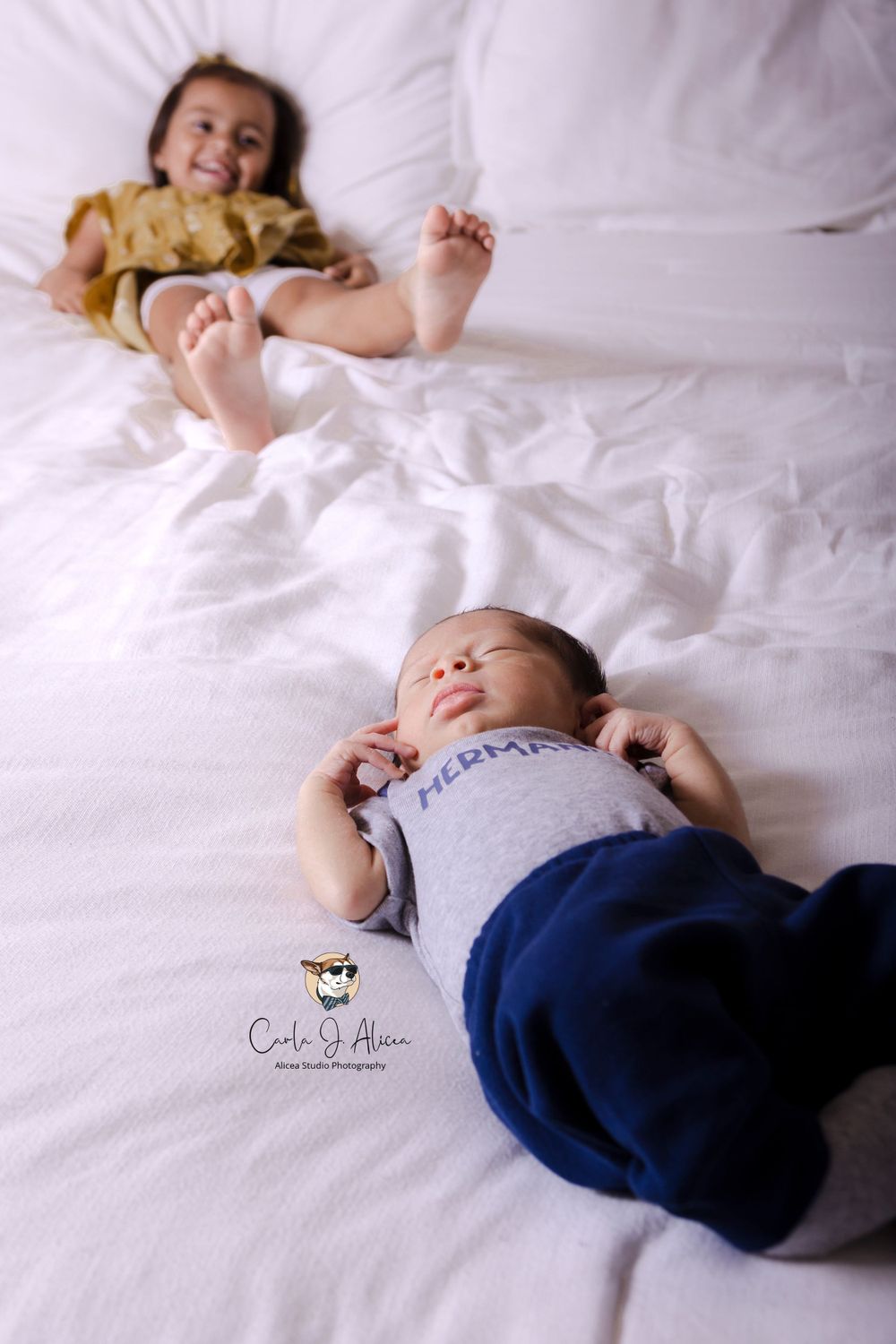 Two children relaxing on white bedding during indoor photoshoot.