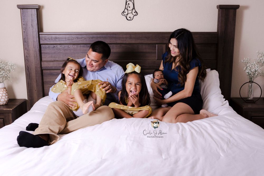 Candid family portrait shows playful interaction between parents and children on bed.