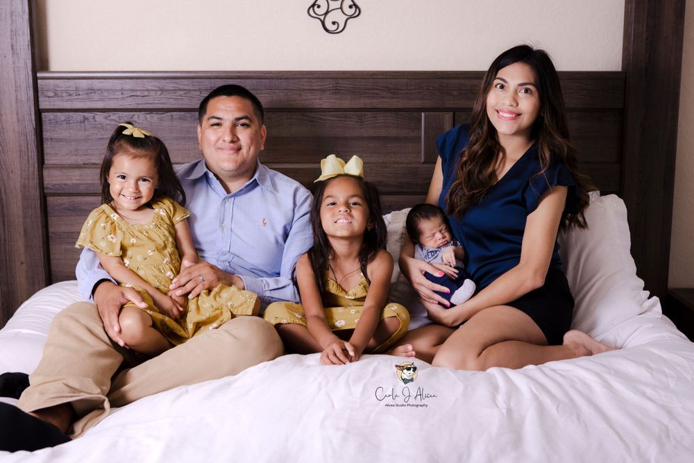 Family of five posing together on bed for indoor studio portrait session.
