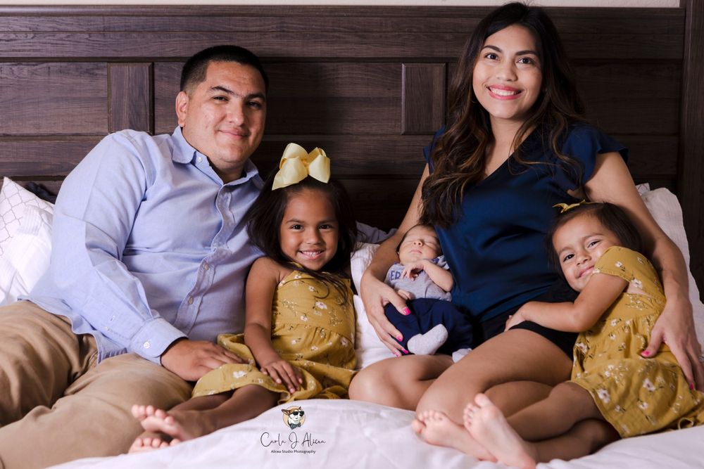 Family of five sharing candid laughs and smiles during bedroom photoshoot session.