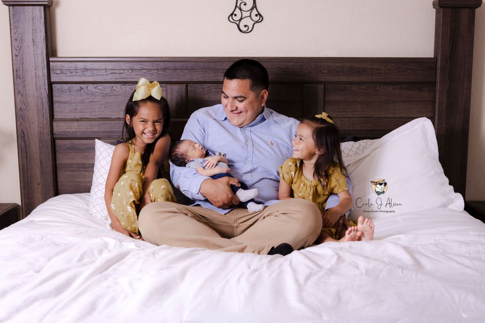 Family shares joyful moment together on white bedding with decorative headboard.