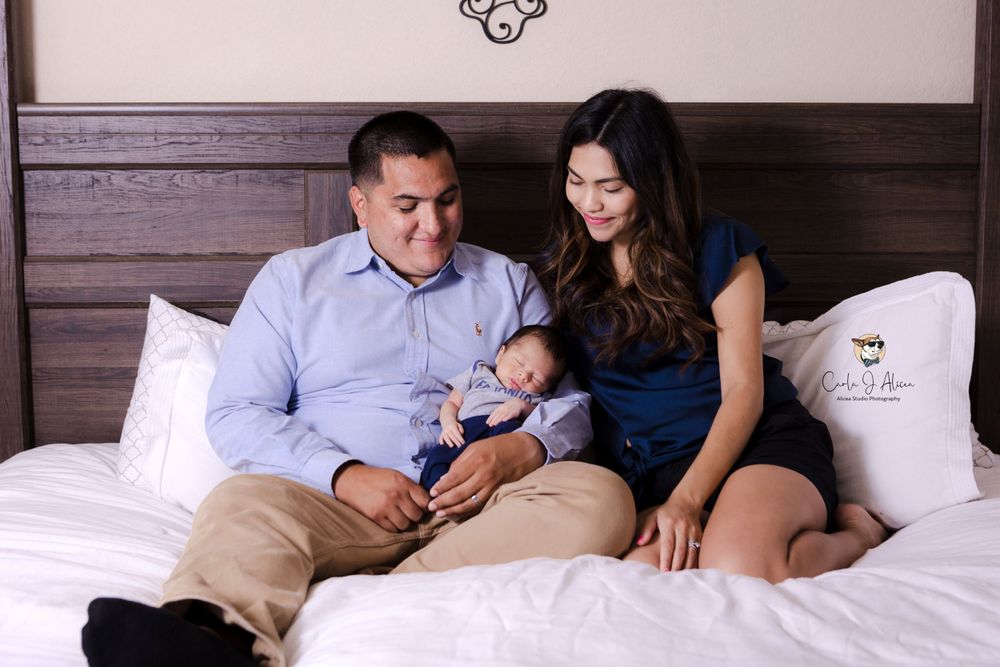 Intimate family portrait on bed with dark wooden headboard and white bedding.