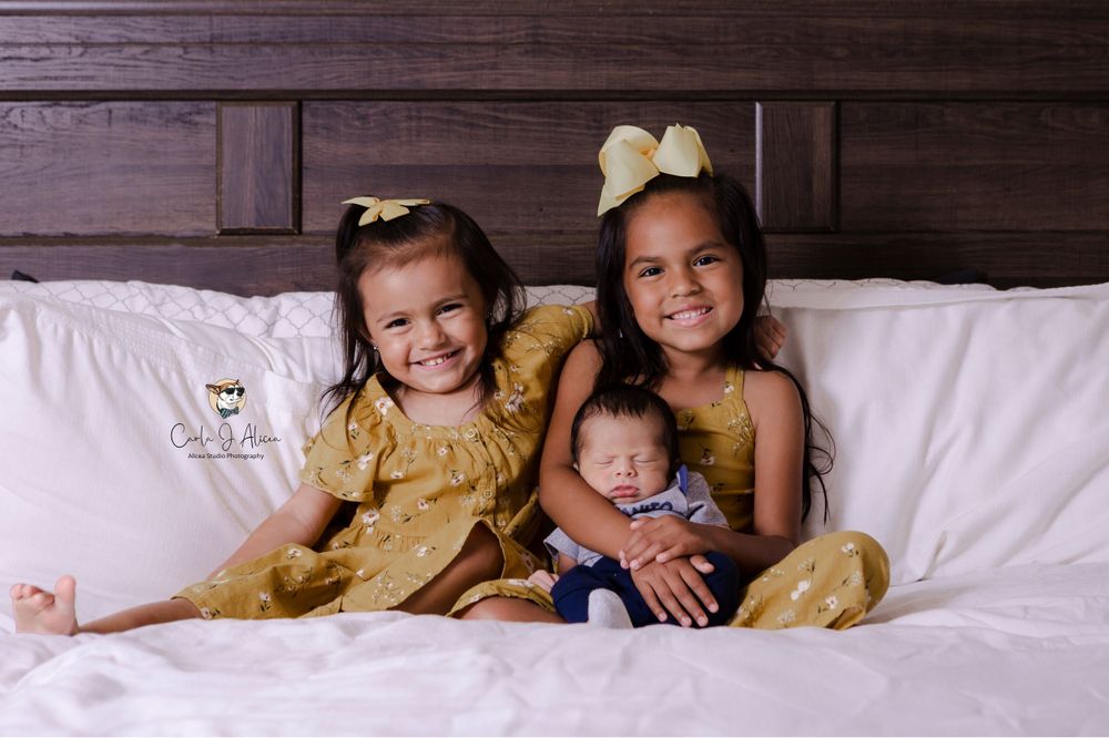 Children in matching gold dresses pose with baby on white bed.