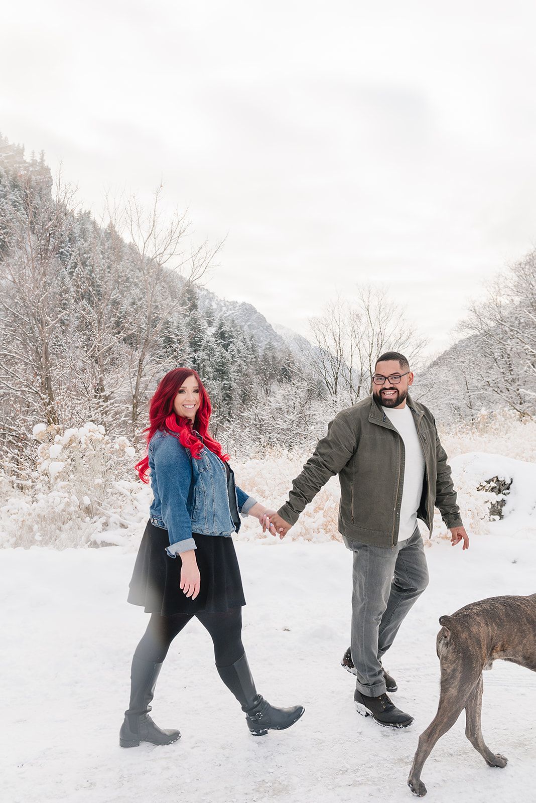 A couple and their dog enjoy a winter walk through snowy mountain terrain.