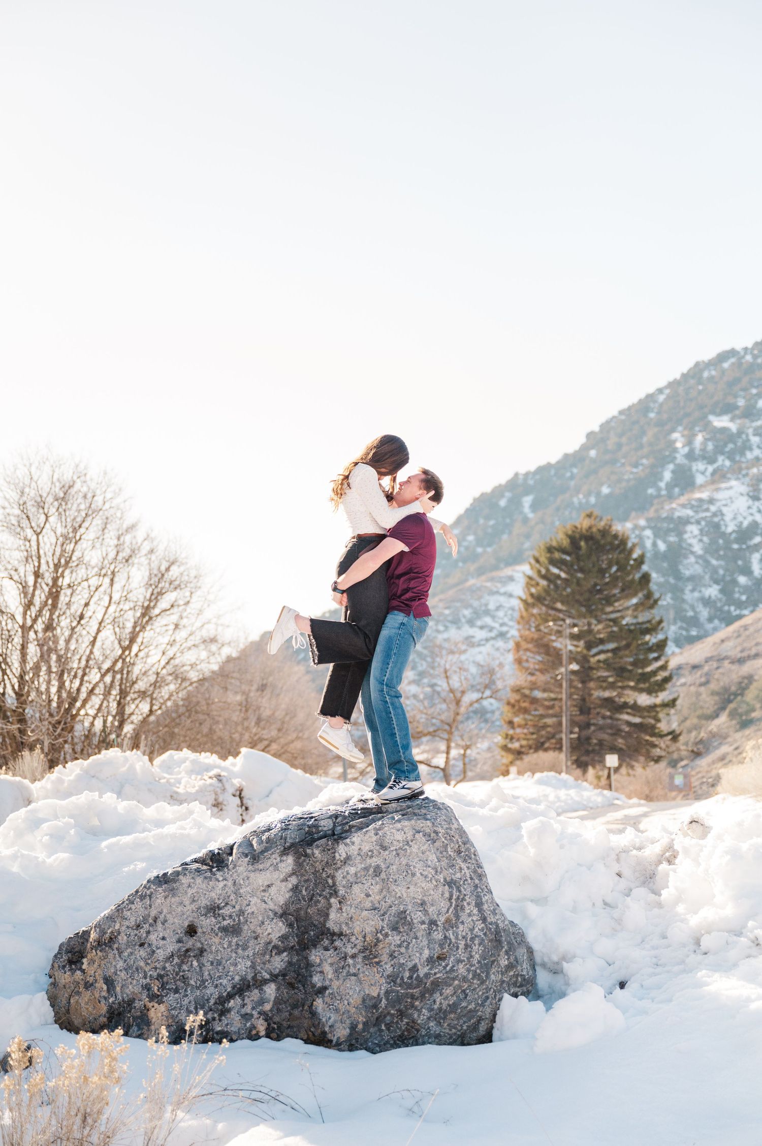 A romantic embrace on a snow-covered boulder with mountain scenery in the background.