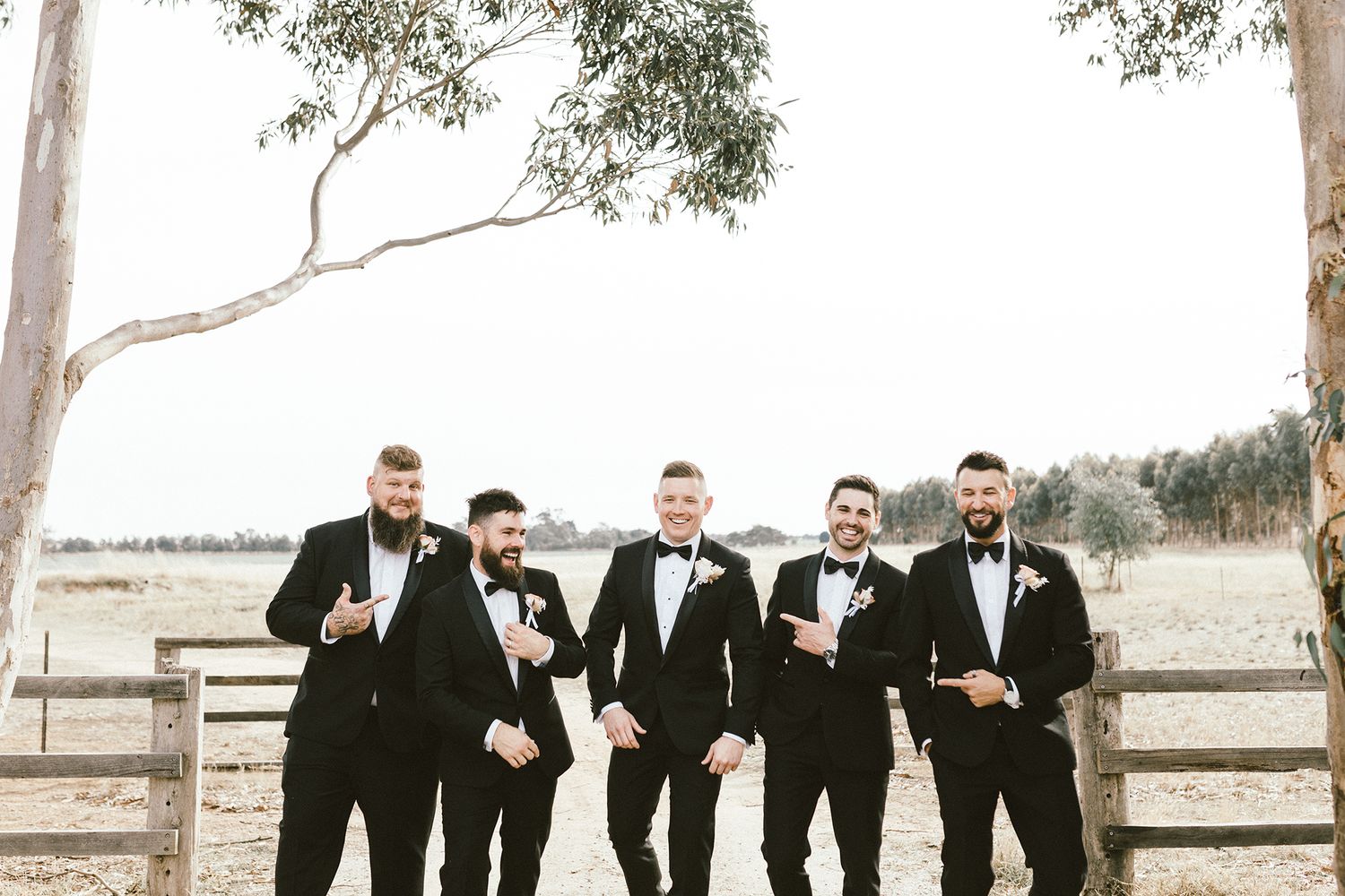 Wedding party in formal attire lined up on a dirt path with eucalyptus trees in the background.
