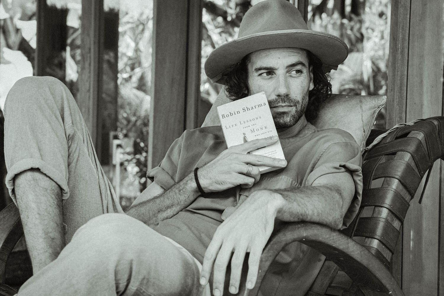 Black and white portrait of person holding book while relaxing in outdoor setting.