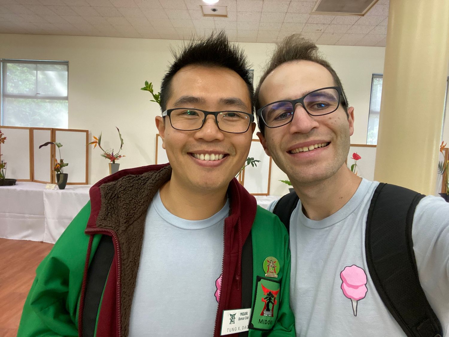 Two people wearing glasses smile at the camera, one in a green jacket and one with a pink Escaype logo on their shirt.