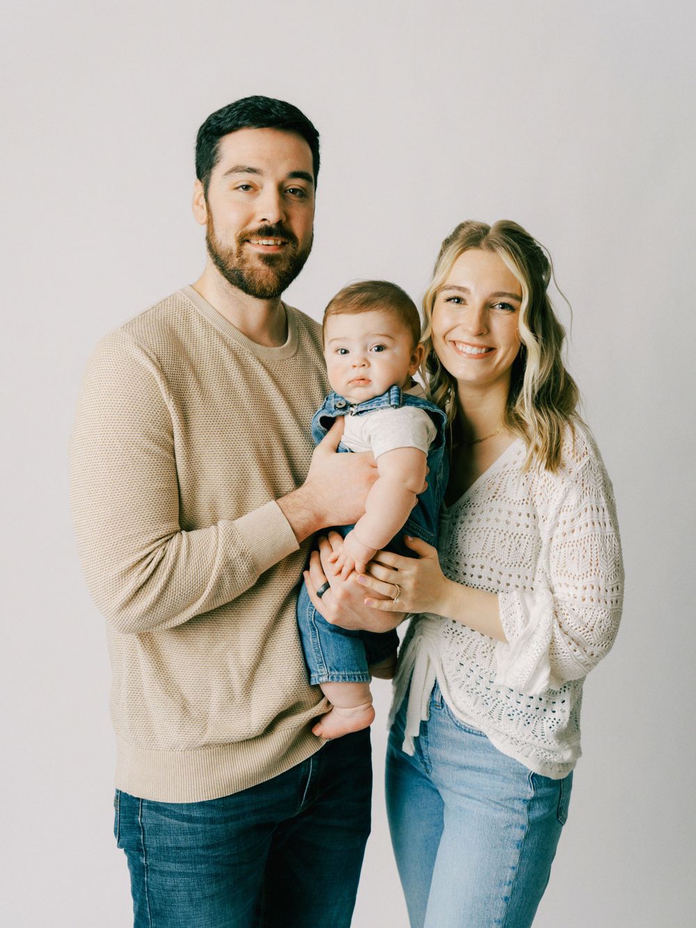 Studio portrait of a family of three wearing casual clothing against a light background.