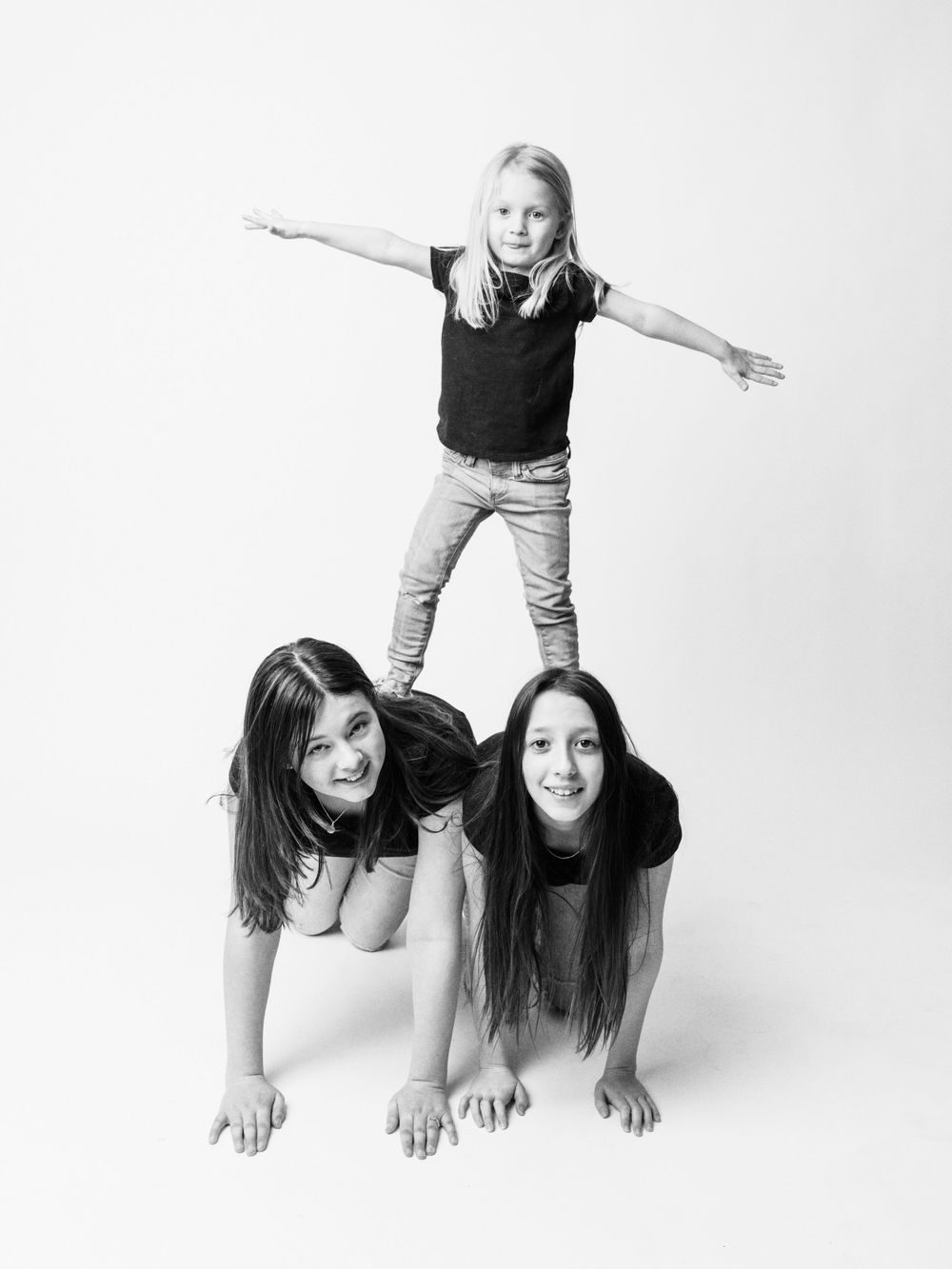 Three people create a playful human pyramid pose against white background.