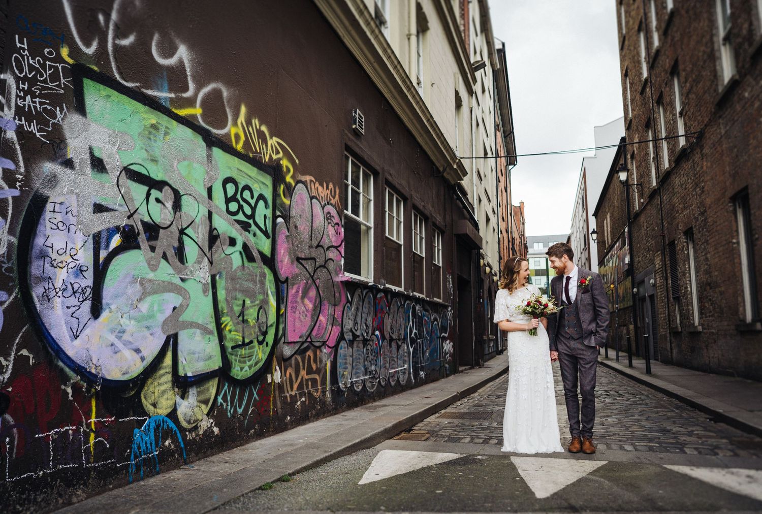 Urban wedding photo with graffiti wall in narrow alley.