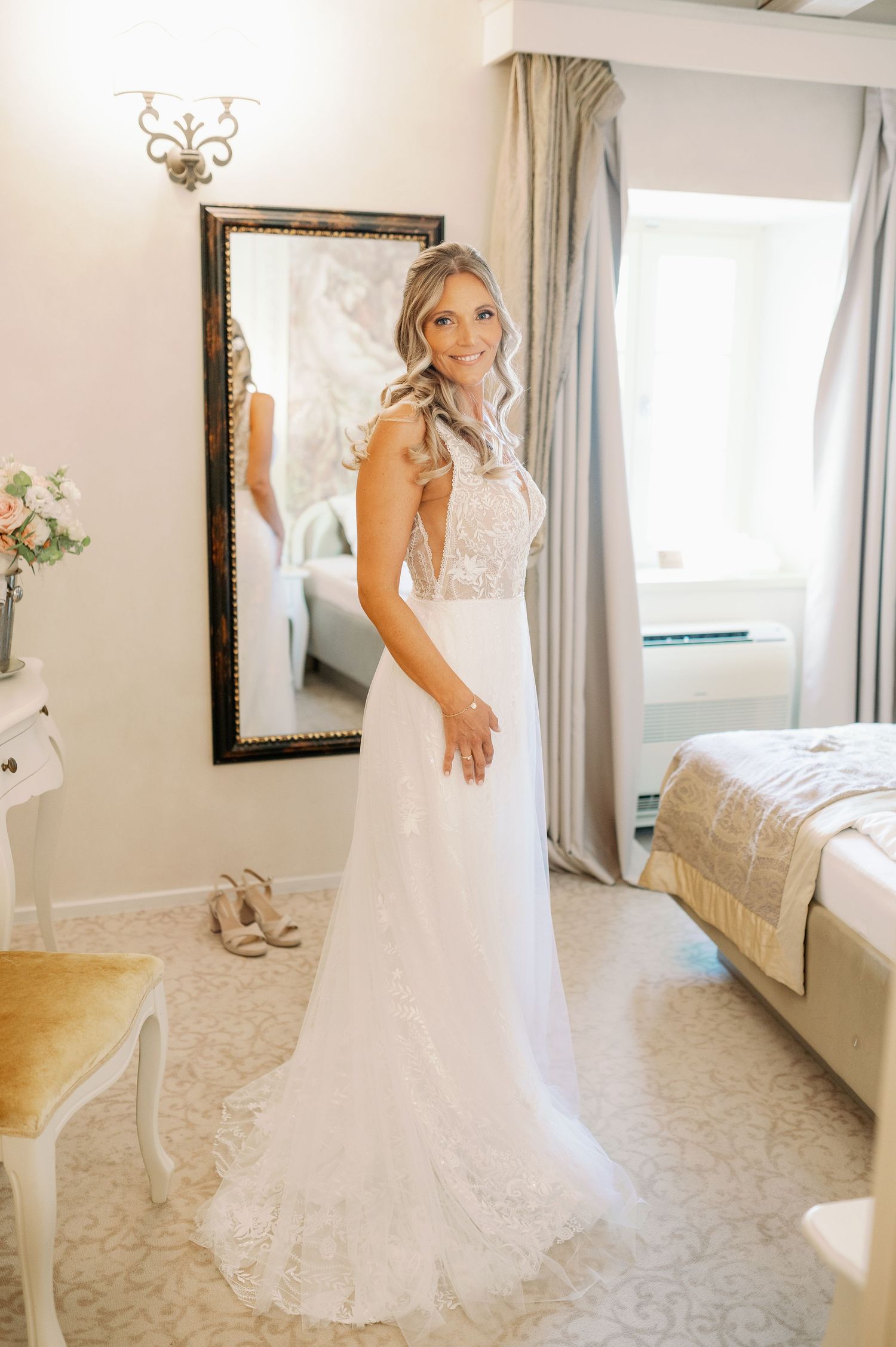 A full-length white lace wedding gown with intricate detailing is displayed in an elegant bridal suite.