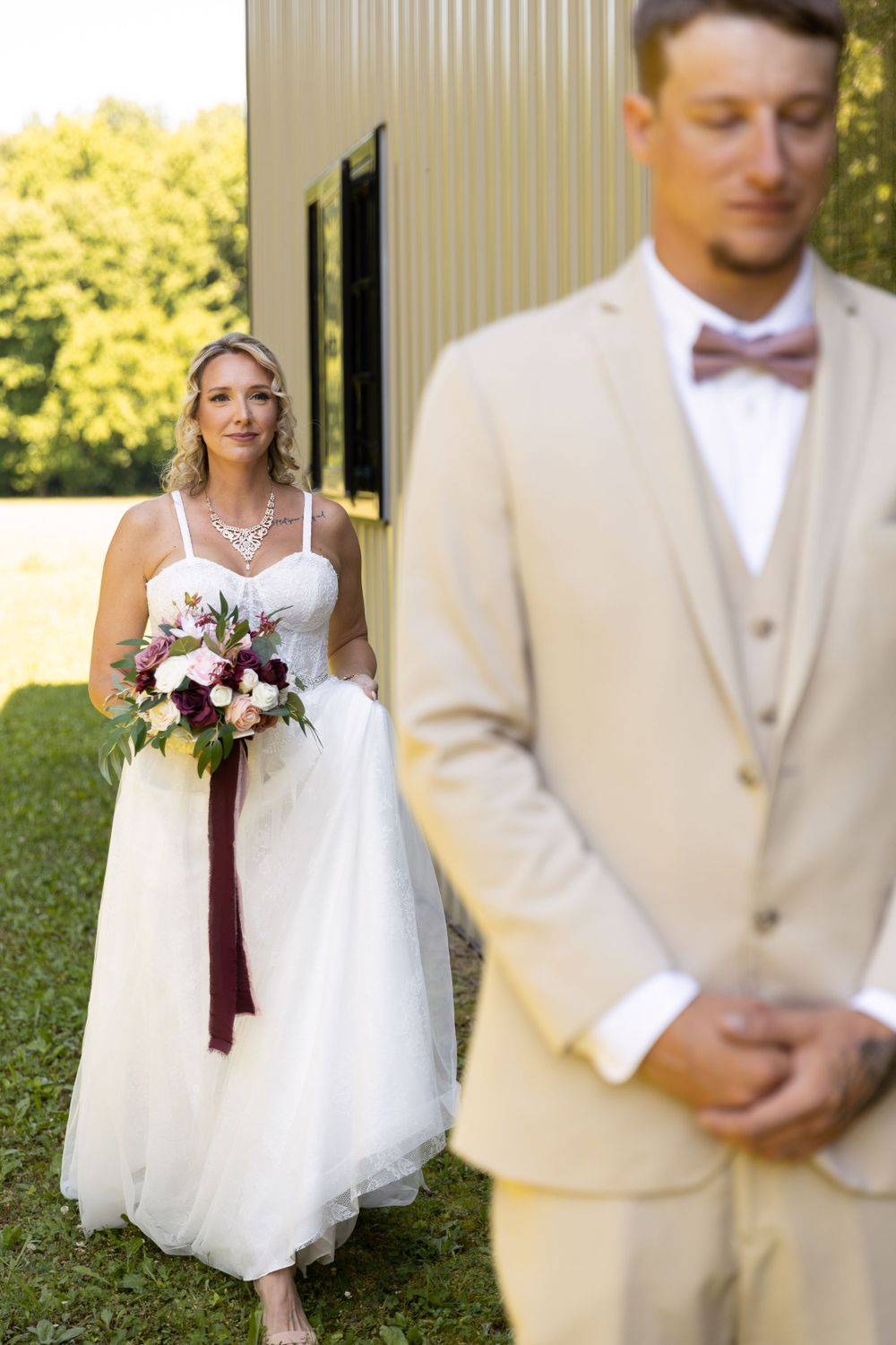 Wedding first look photos with couple in cream suit and white dress holding burgundy bouquet.