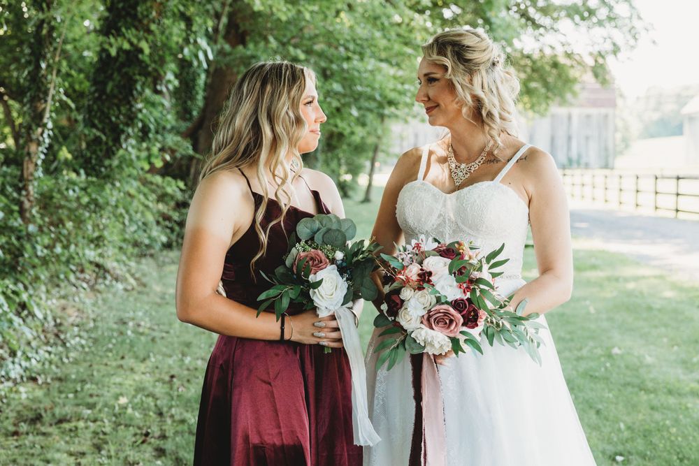Wedding party members pose with floral bouquets in burgundy and white dresses.
