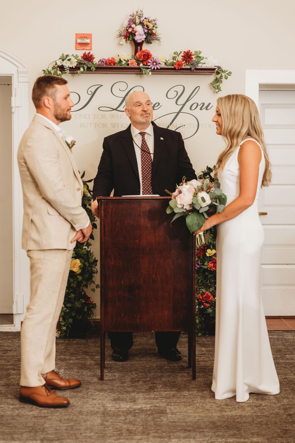 Wedding ceremony setup with wooden podium and floral decorations against white backdrop. Annapolis courthouse wedding photography