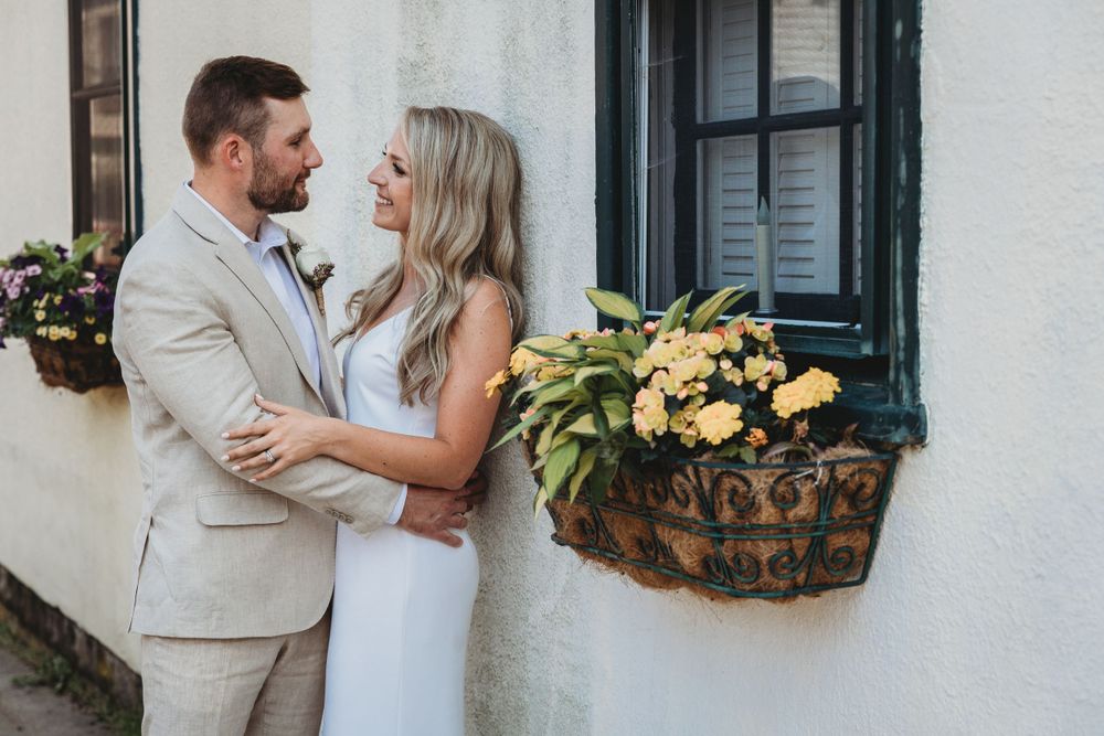 Couple poses against white stucco wall with blue shutters and window boxes in downtown annapolis. Annapolis Wedding photographer