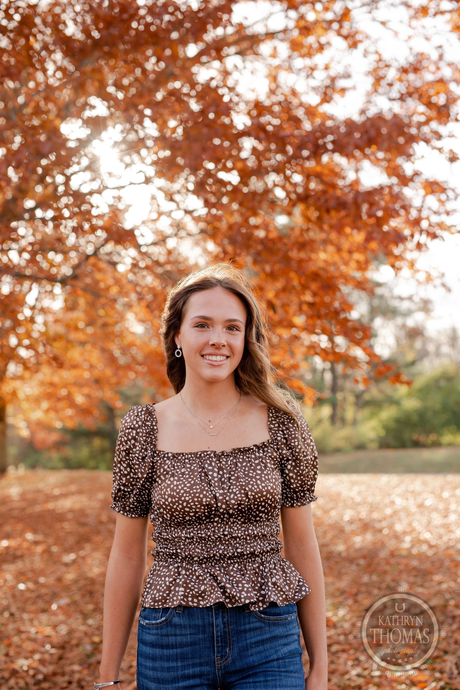 A portrait in a leopard print top against a backdrop of autumn trees with golden leaves.