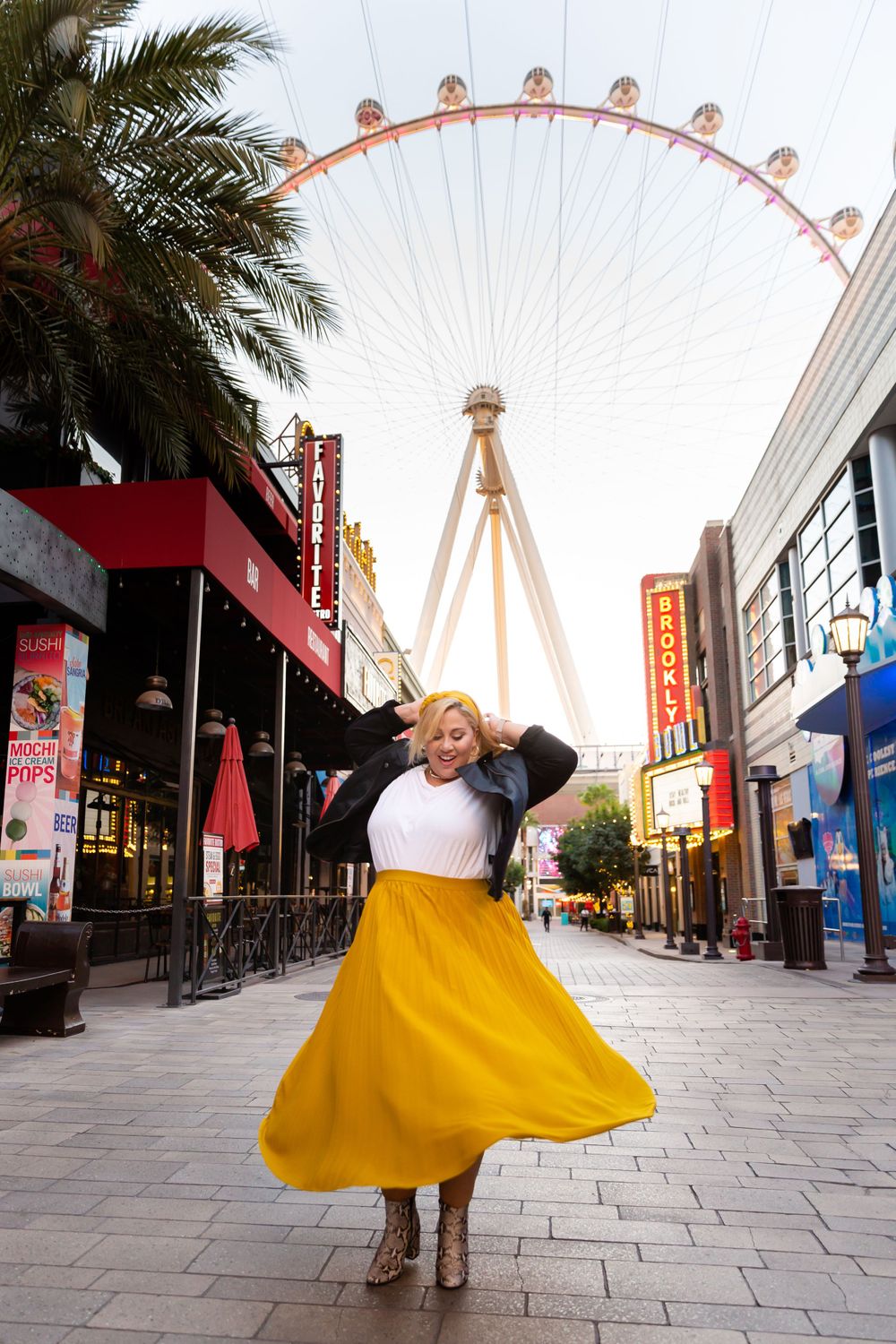 A vibrant yellow skirt swirls in front of the High Roller observation wheel at The LINQ promenade in Las Vegas.