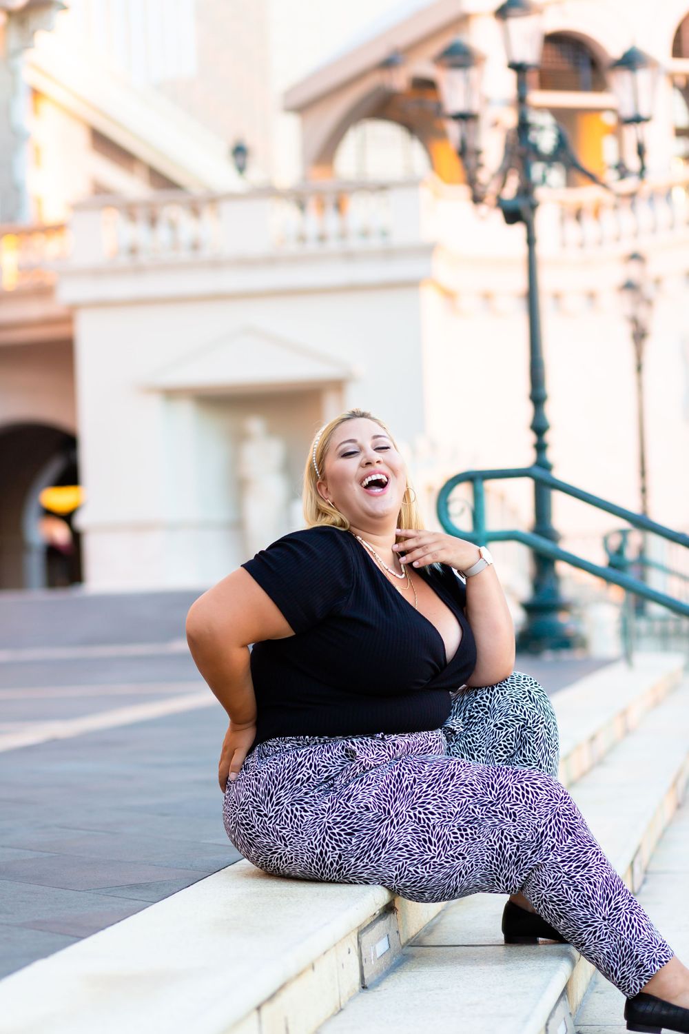 Joyful fashion portrait on stone ledge with architectural columns in background.