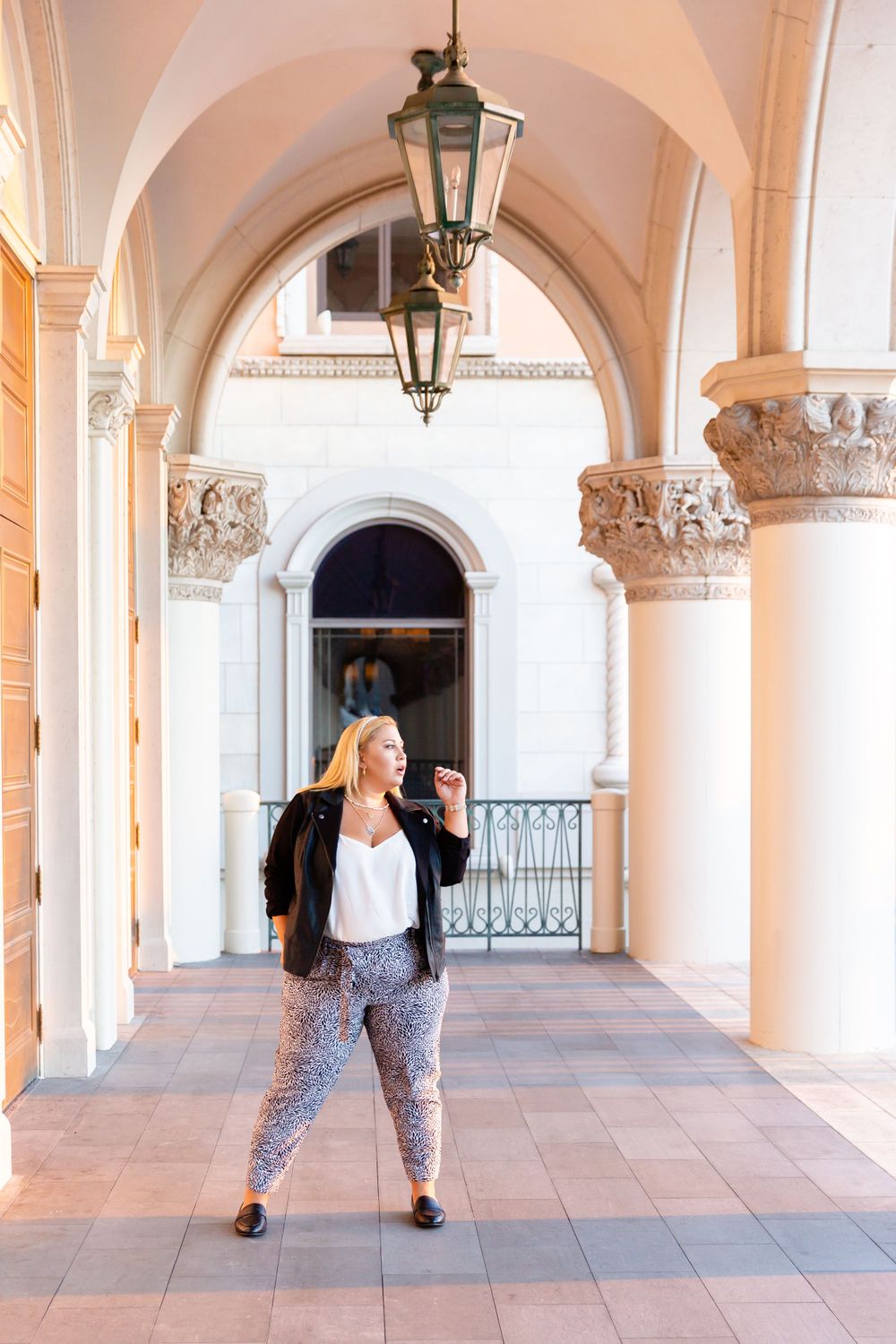 Casual portrait under arched colonnade with decorative capitals and hanging vintage lantern.