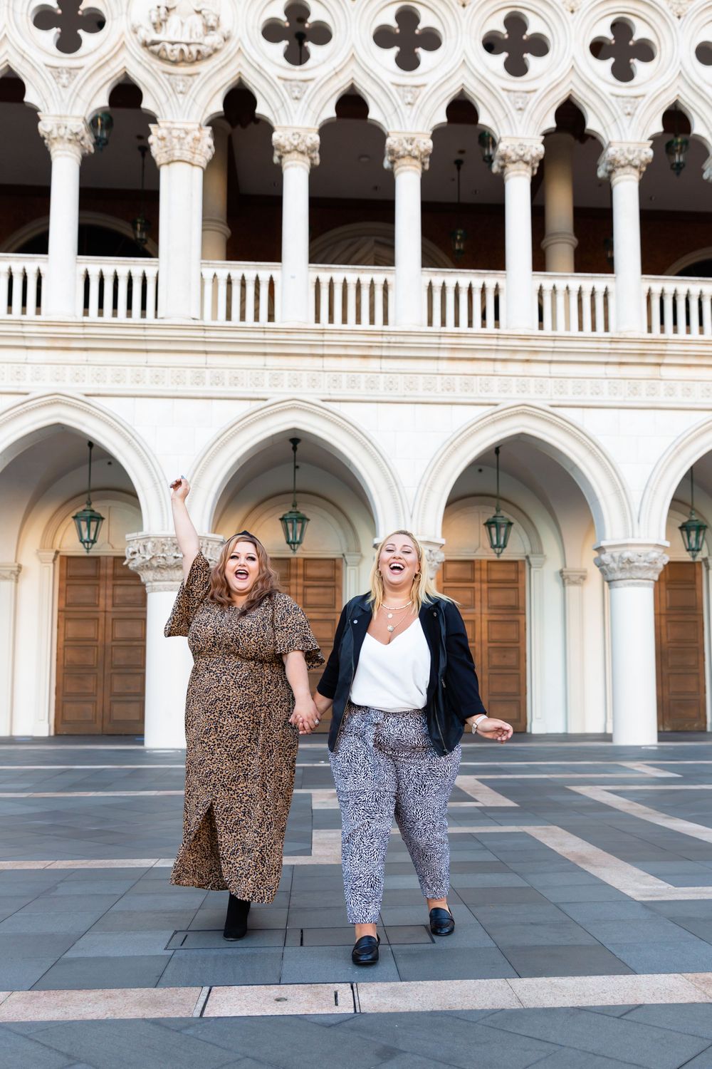 Two visitors pose against stunning Gothic architecture with ornate columns and arched doorways.
