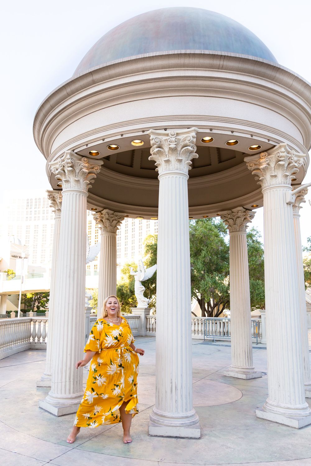 Bright yellow floral dress creates striking contrast against white classical columns of an ornate gazebo.