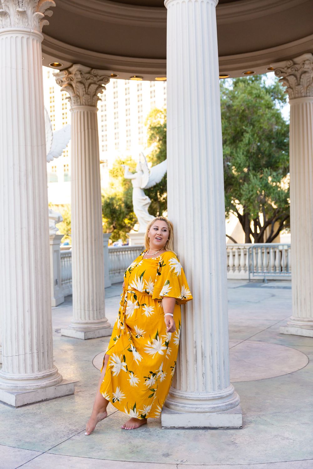 A bright yellow floral maxi dress contrasts with classical white columns in an architectural setting.