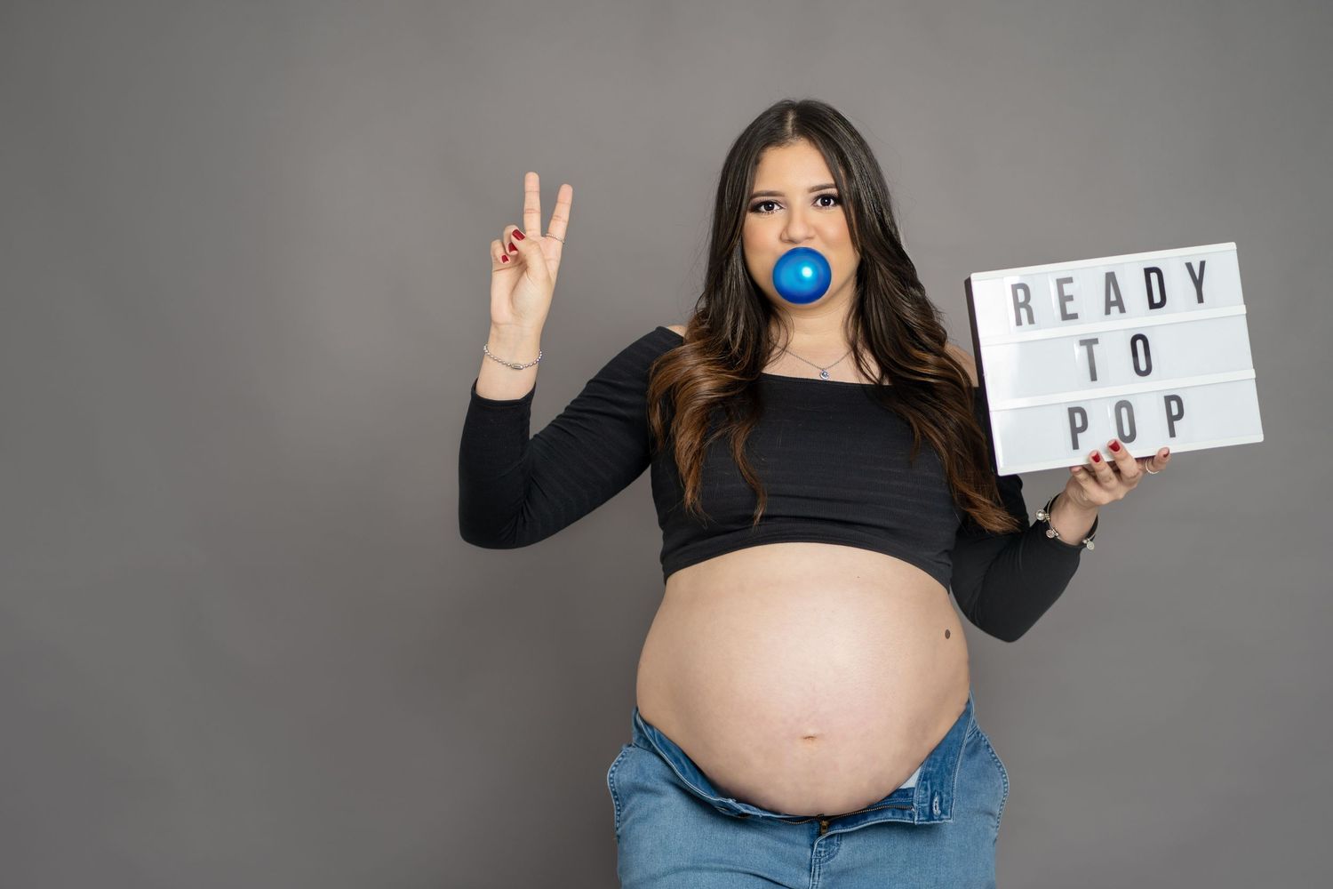 Expectant parent holding sign reading Ready to Pop while making peace sign.