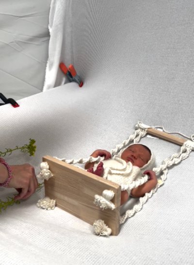 A tiny wooden prop bed with white lace trim holds a sleeping baby during a photography session.