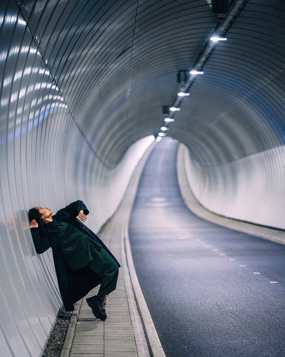 Figure in black coat striking dramatic pose in curved white tunnel.