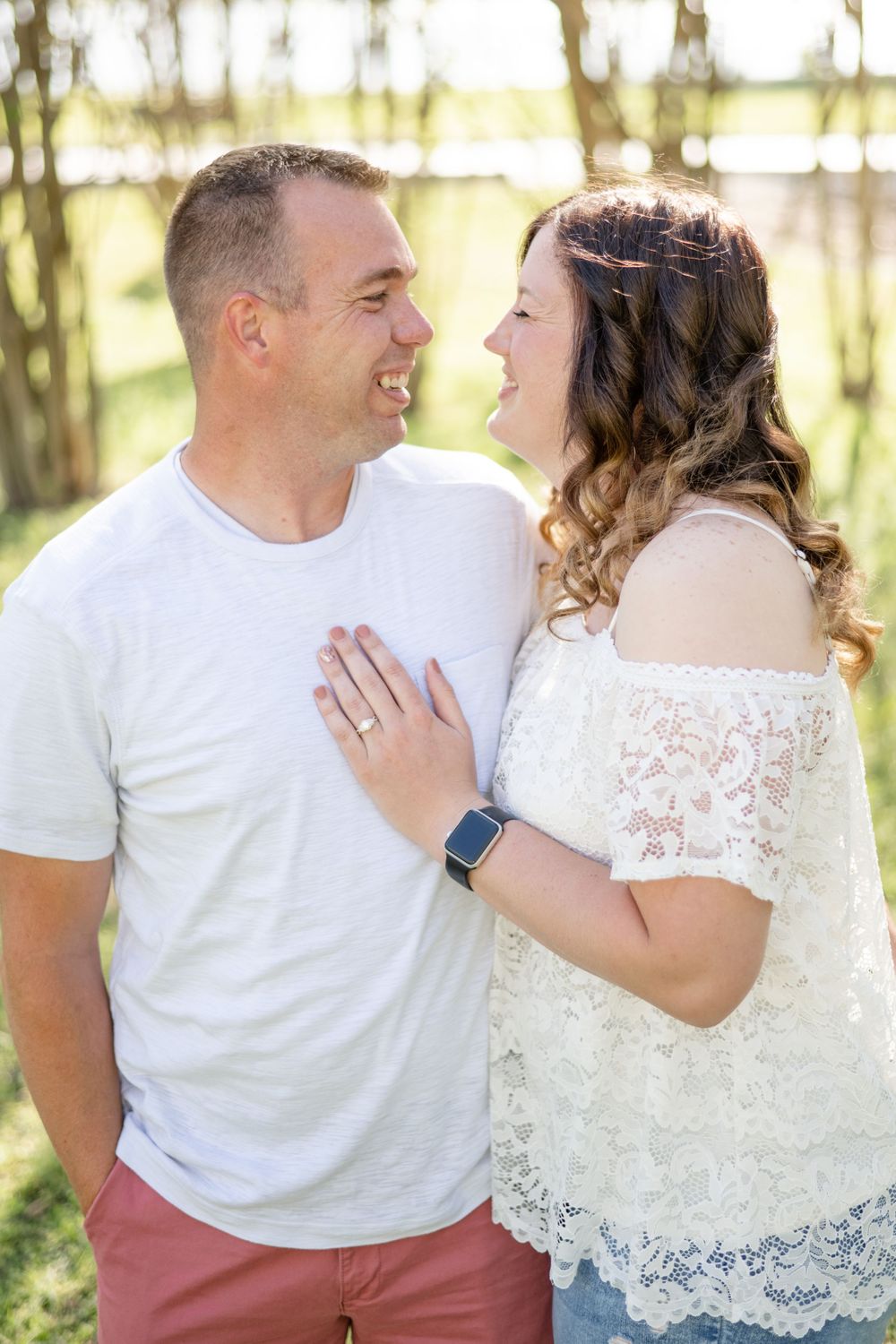 A couple in casual attire sharing a joyful moment in a sunlit forest setting.