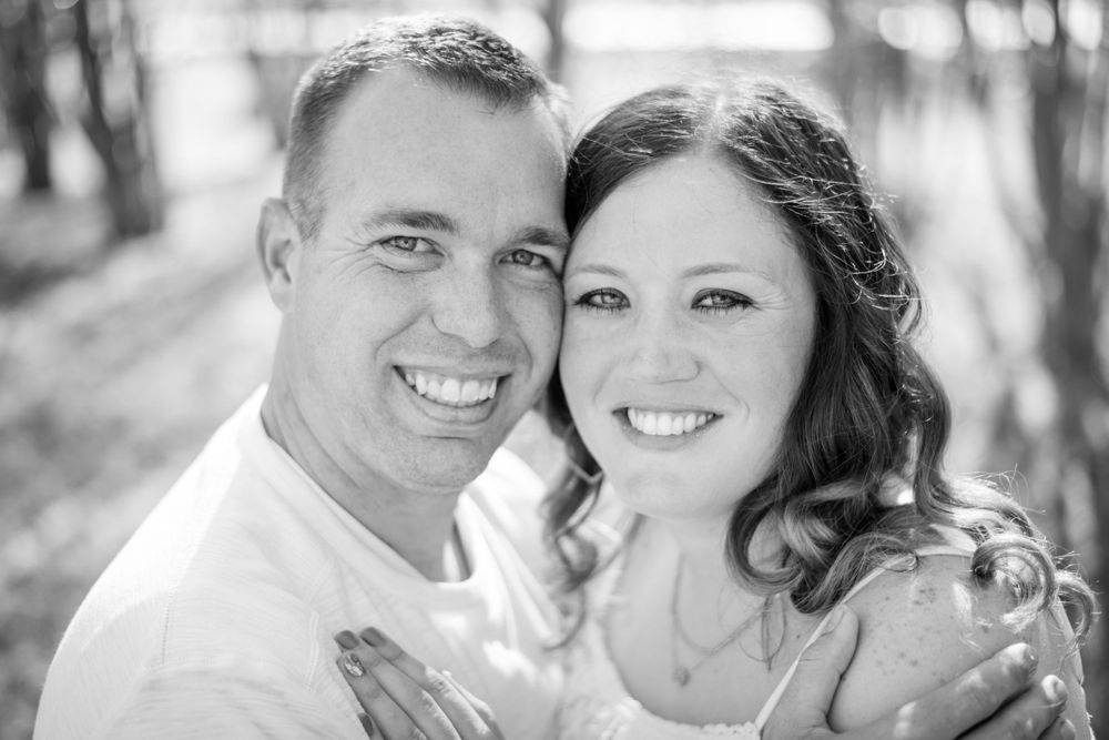 A close-up portrait of a happy couple smiling outdoors in black and white.