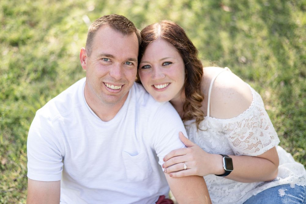 A couple in white clothing sitting together on grass during an outdoor photo session.