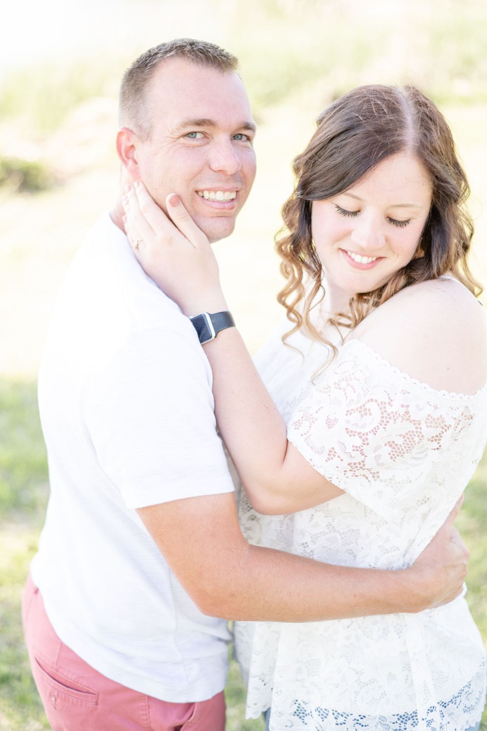 A romantic couple embracing in soft sunlight during an outdoor photo session.