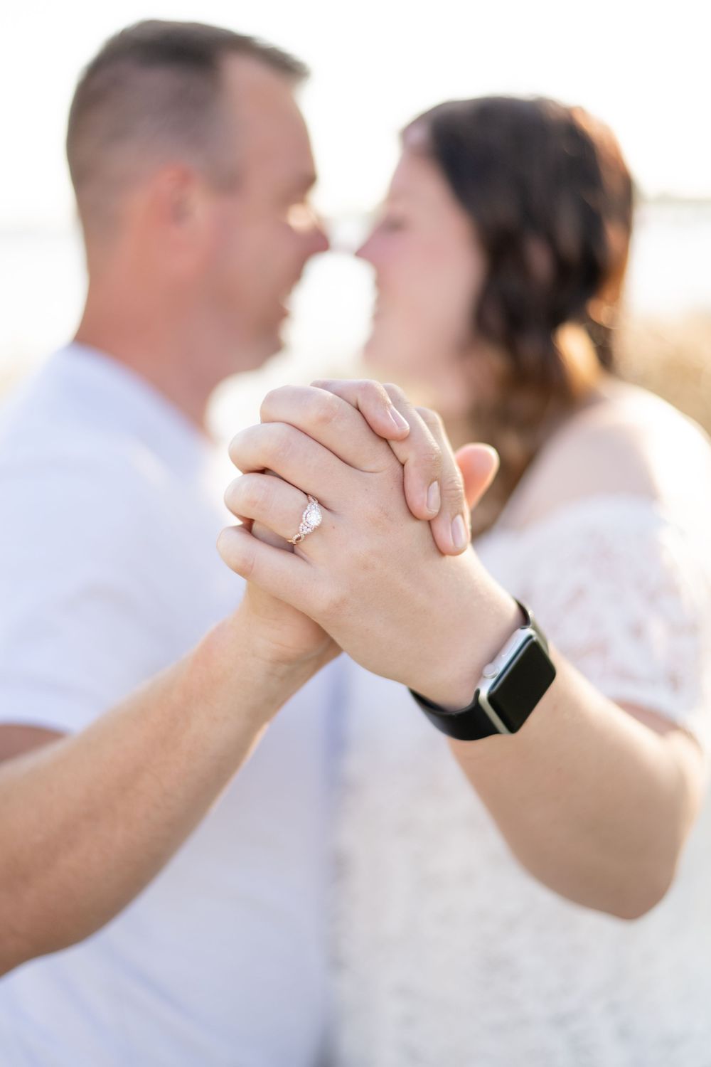 Close-up of clasped hands showing engagement ring and smartwatch during romantic moment outdoors.