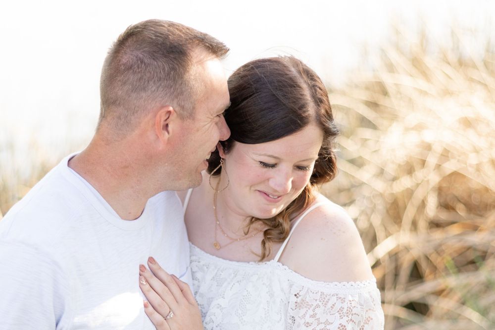 Romantic couple in white clothing embracing against sunlit wheat field background.