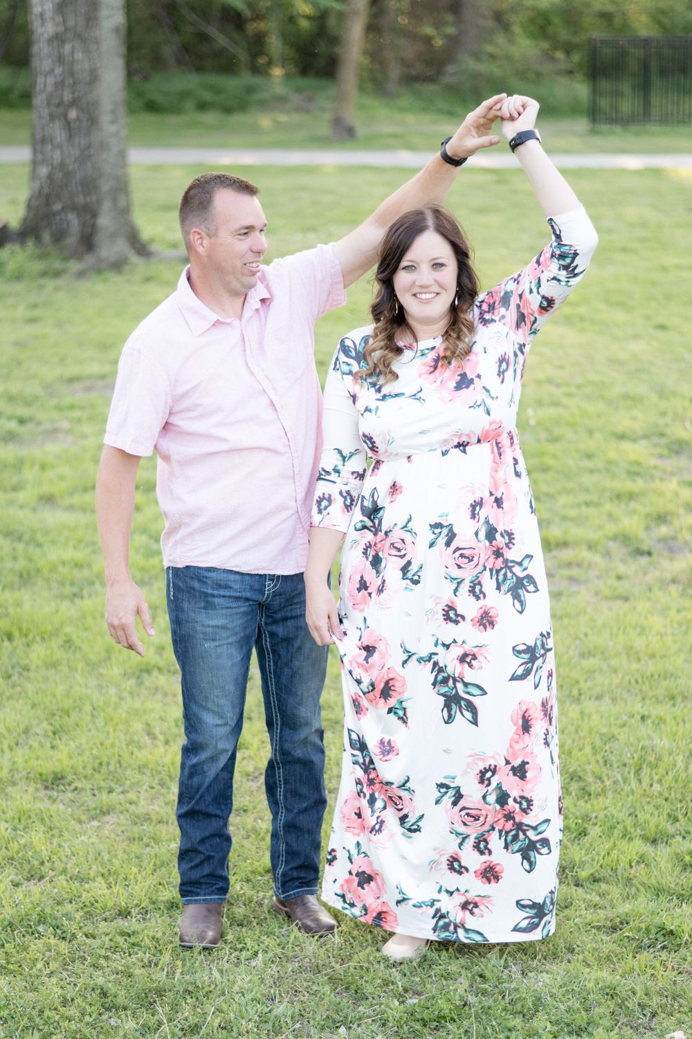 Dancing couple in casual attire enjoying moment on green lawn during photoshoot.