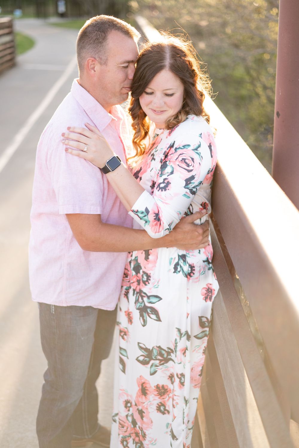 Intimate portrait of couple embracing on bridge pathway during golden hour.