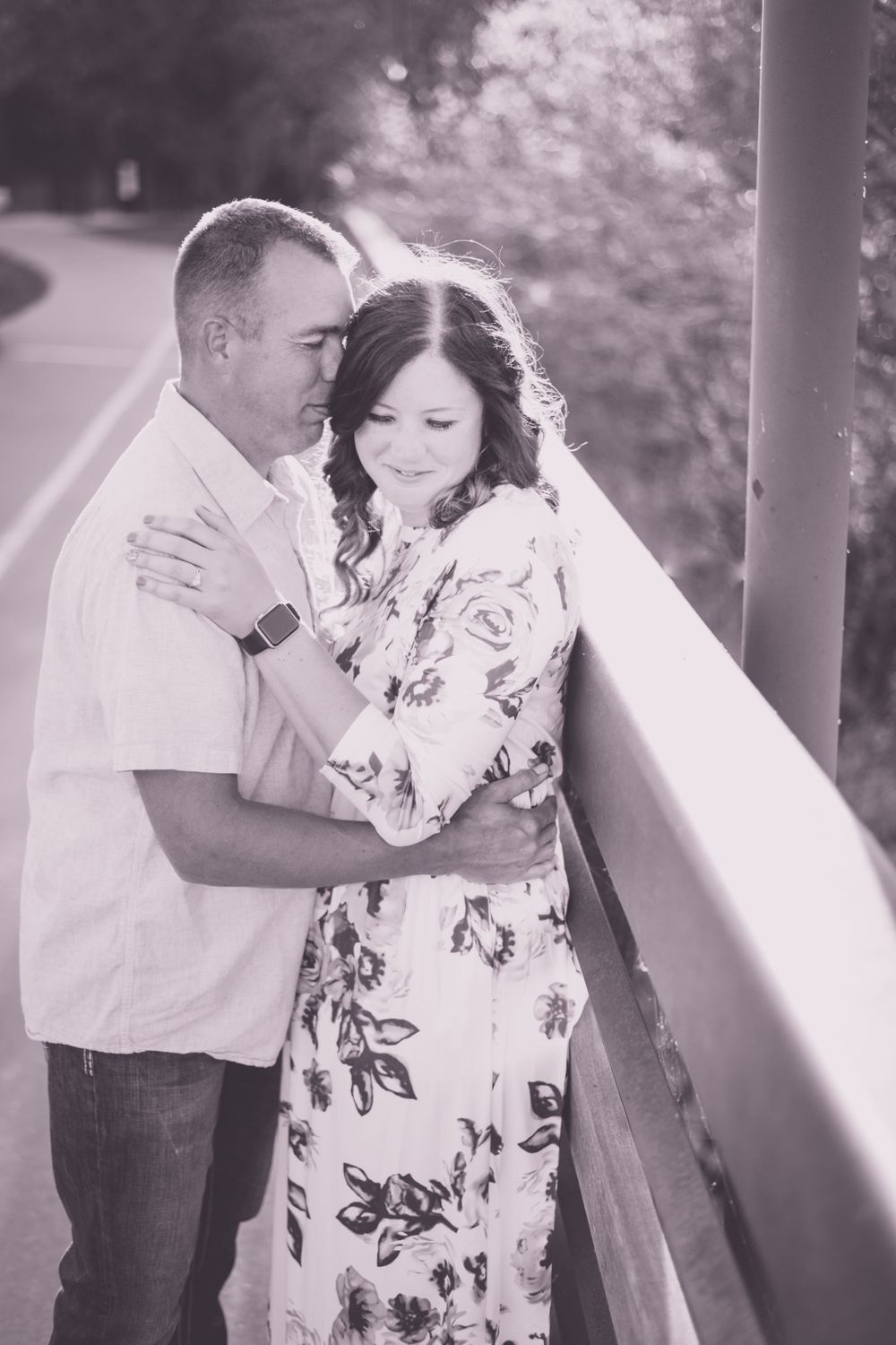 Black and white romantic portrait of couple embracing on bridge walkway.