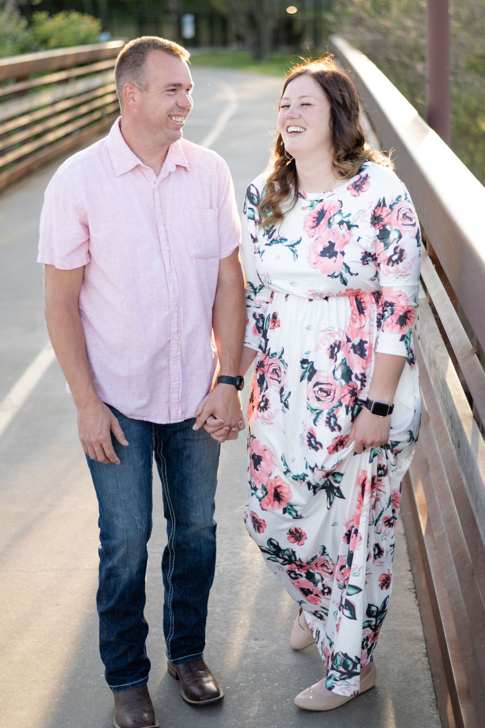 Candid moment of couple laughing while walking together on wooden bridge pathway.