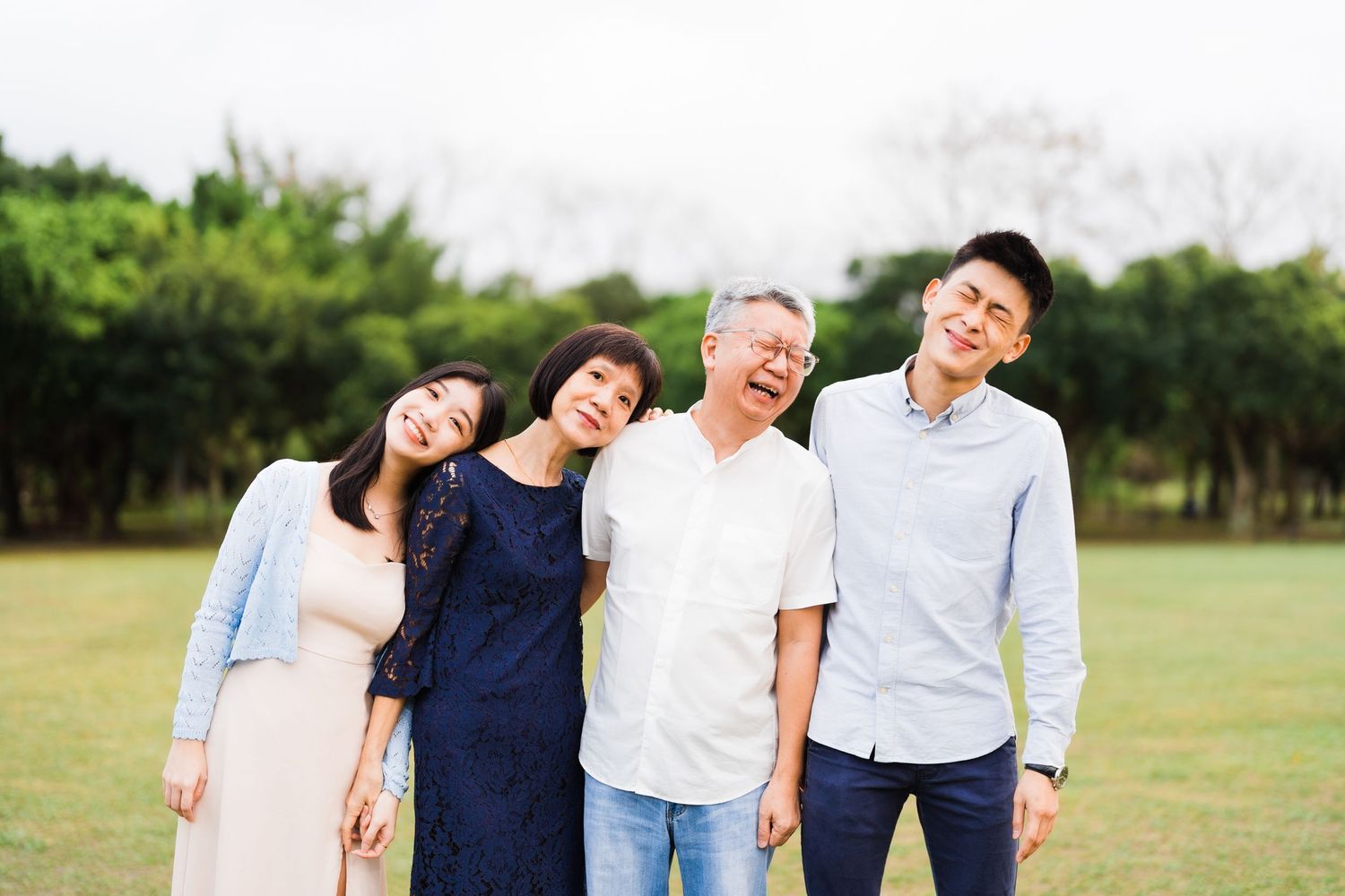 A joyful family portrait taken outdoors in a park with trees in the background.