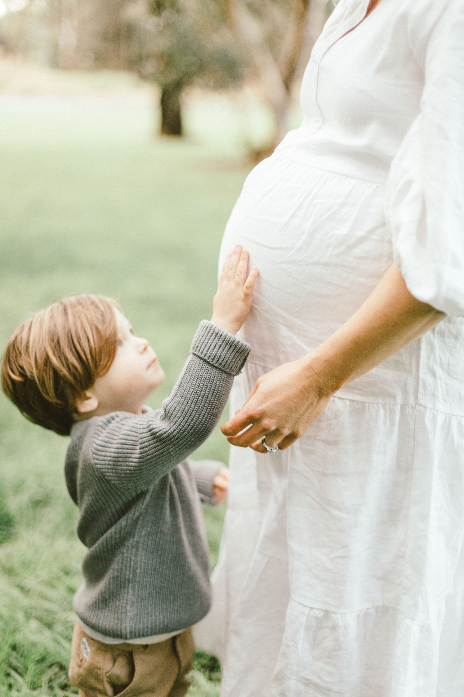 Tender moment between child and expectant mother during outdoor maternity photoshoot.
