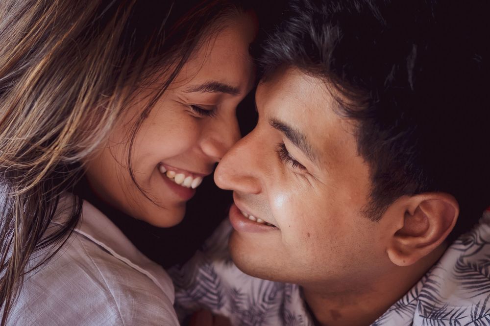 Close up intimate portrait of a couple sharing a tender romantic moment while smiling and touching foreheads.
