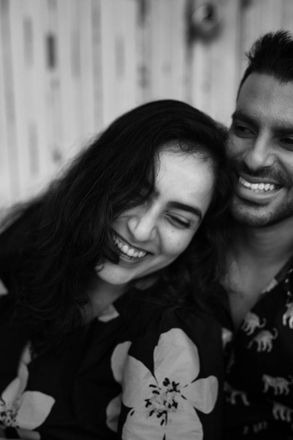 A black and white close-up portrait of a smiling couple with white flowers in the foreground.