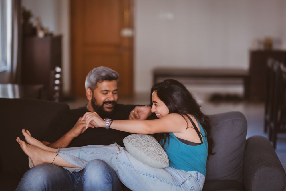 A couple relaxes together on a gray couch in their living room, sharing a tender moment of laughter and connection.