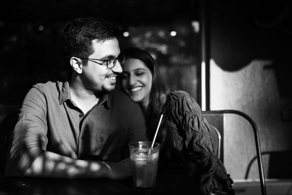 A couple shares an intimate moment in black and white while sitting at a dimly lit bar with drinks.