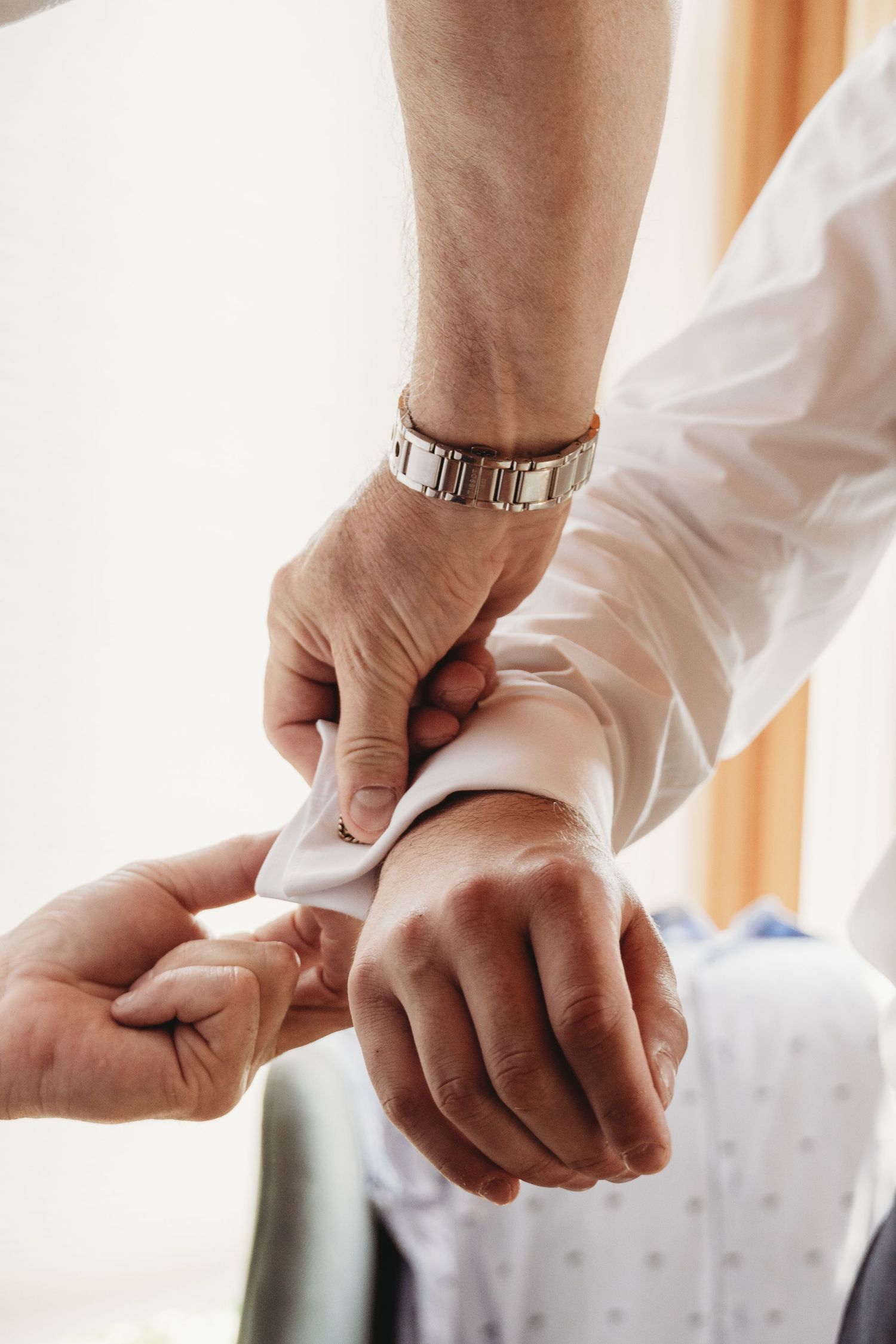 Close-up shot of hands adjusting white shirt cuffs with a silver watch visible.