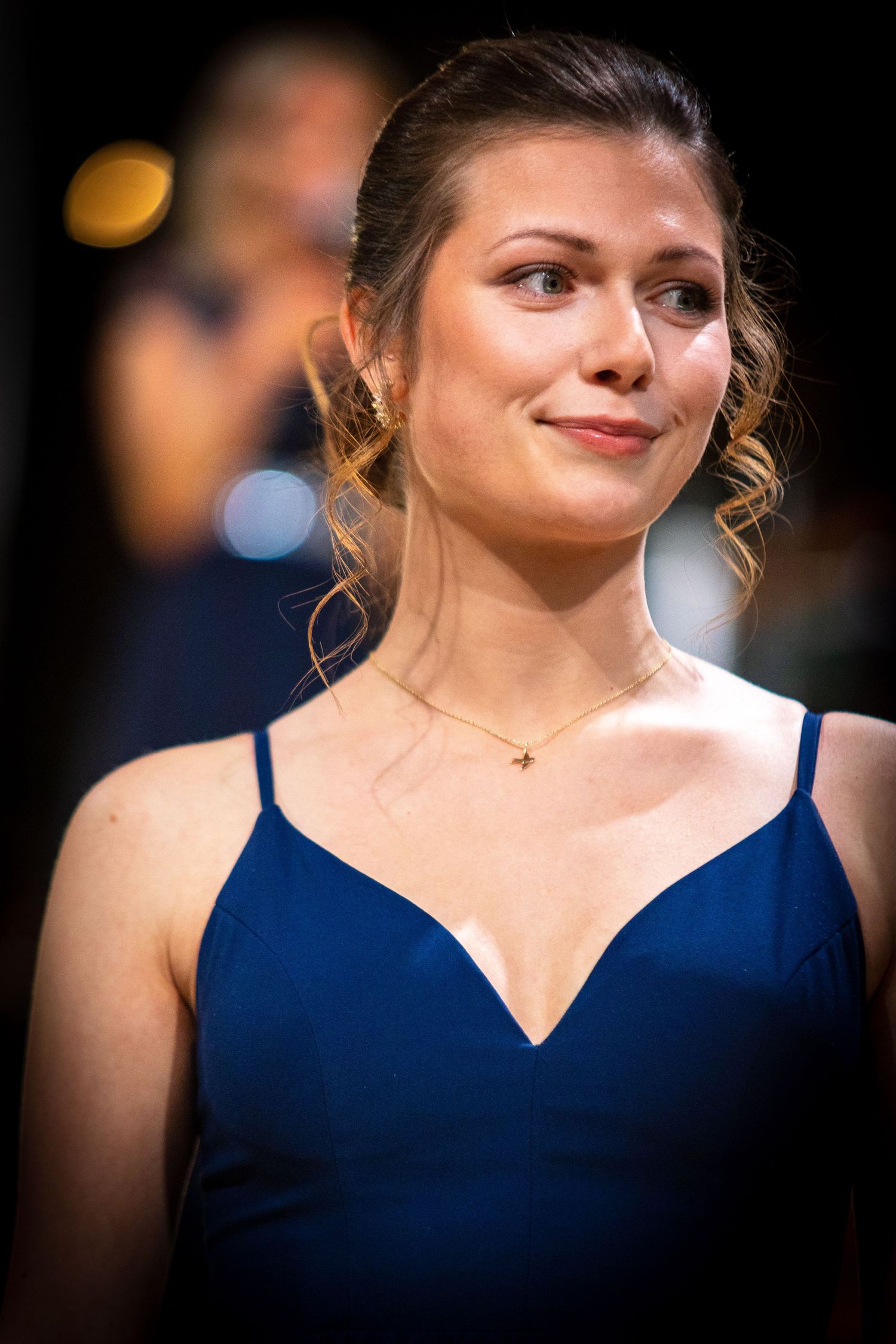 Elegant young woman in a blue spaghetti strap gown with gold necklace at a formal event.